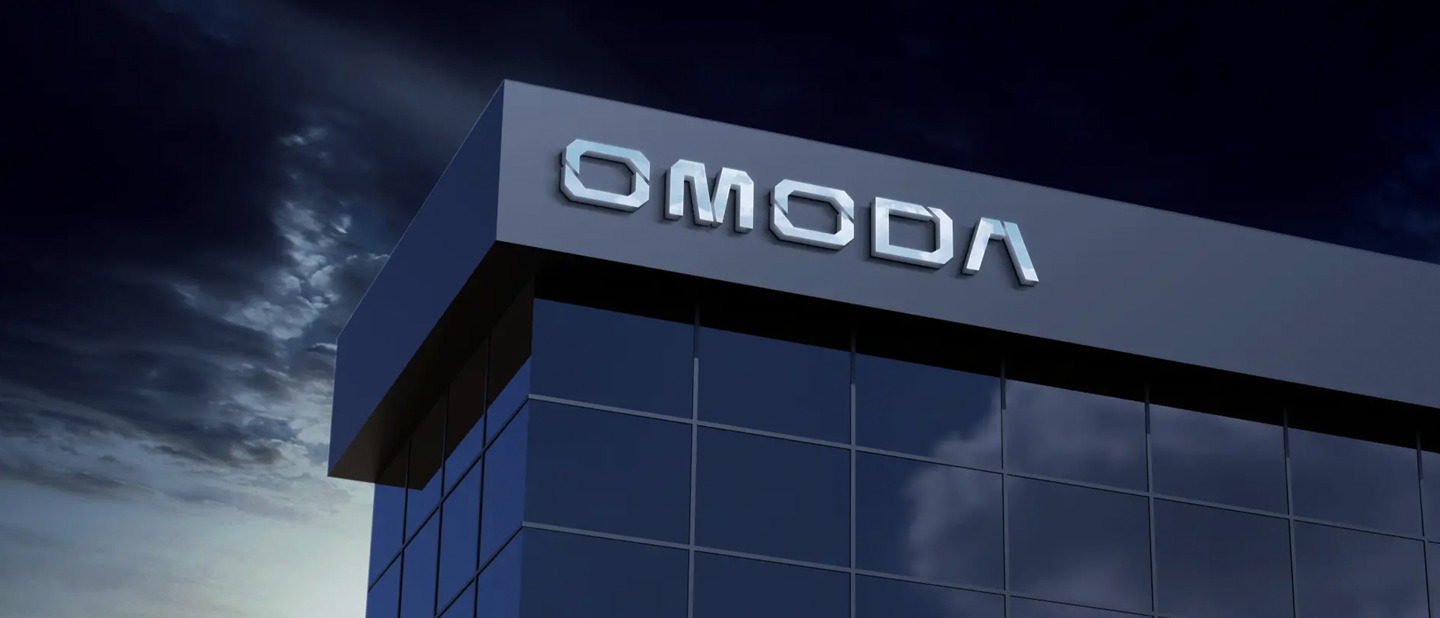 En moderne glasbygning med OMODA i store bogstaver på facaden mod en overskyet aftenhimmel.